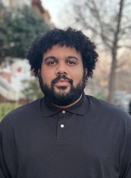 A man with a beard and curly hair is wearing a black polo shirt.