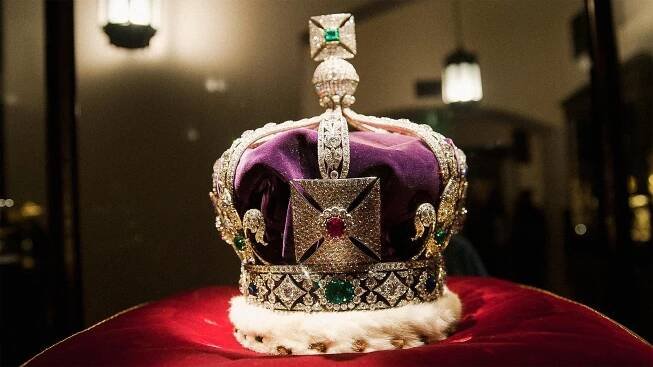 Crown with purple material and gems atop red cushion