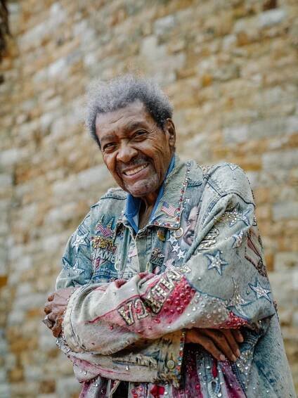 Don King posing in a denim jacket decorated in rhinestones, American flags, stars and stripes. 