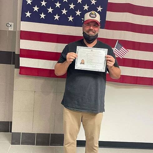 Tyler Labine smiles while holding his citizen certificate and an American flag in 2021