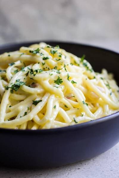 a big serving of creamy pancetta carbonara in a bowl with fresh italian parsley on top