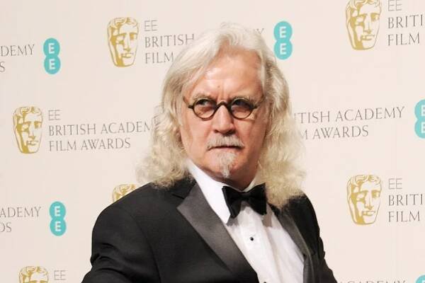 a man in a tuxedo stands in front of a wall that says british academy film awards