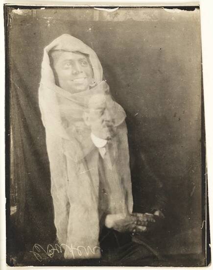 photograph of seated man with the translucent apparition of a man draped in white above his head