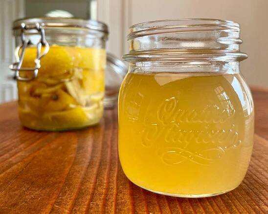 A jar of lemon rind syrup sits in the foreground. In the background in a jar of lemon rind soda at the start of fermentation.