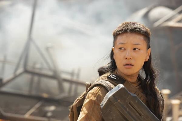Kwan Ha stands with a UNSC Assault Rifle, previously used by Master Chief, while twisting rubble smokes in the background.