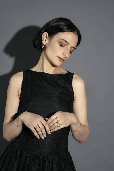 jenny slate poses with her eyes closed and hands touching while wearing her hair in a bob and a black dress in a press shot
