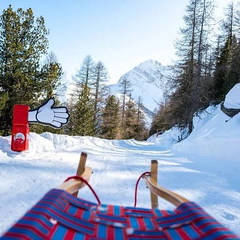 View from the sled on the interactive sledding run Hannig in Saas-Fee, Valais, with story stations about marmot Eddie and a snowy mountain landscape in the background.