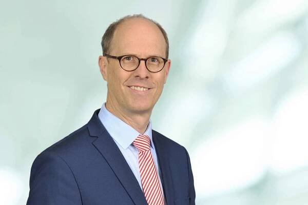 Ein Mann in einem blauen Anzug mit einem rot-weiß gestreiften Krawatte steht vor einem hellen, verschwommenen Hintergrund. Portrait von Dr. Michael Müller.