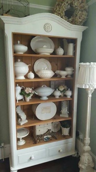 a white china cabinet with plates and vases on it's shelves next to a lamp
