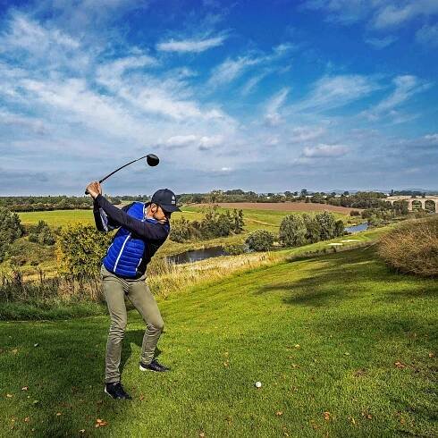 Golfer swinging a club on a lush golf course landscape.