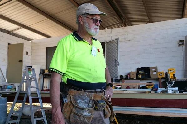 Chris Jacobs standing in a fluoro shirt with a tool belt and hand on his hip. 