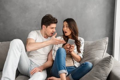 nespokojený pár sedící společně na pohovce doma, zatímco muž křičí na ženu, která drží smartphone v ruce, izolovaná nad bílým pozadím - man fight technology - stock snímky, obrázky a fotky