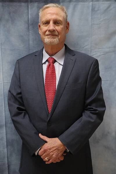 A man in a suit and tie is standing with his hands folded