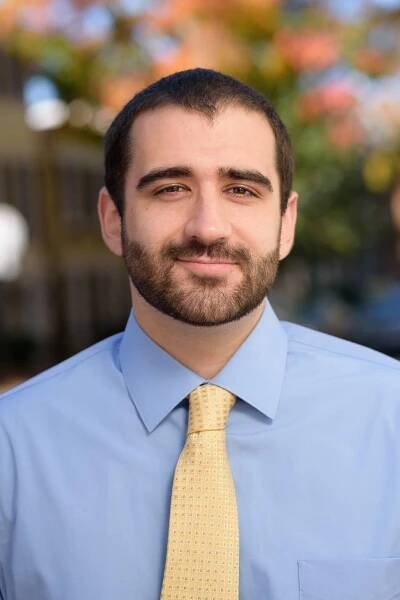 A man with a beard is wearing a blue shirt and a yellow tie.