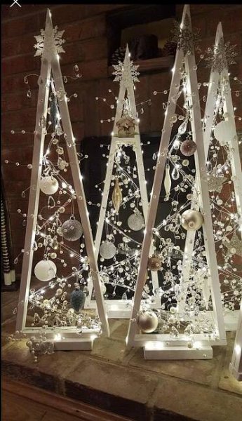 three christmas trees made out of glass with lights and ornaments on them in front of a fireplace