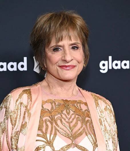Patti LuPone on red carpet in an elegant, patterned gown, smiling at an event with "GLAAD" in the background