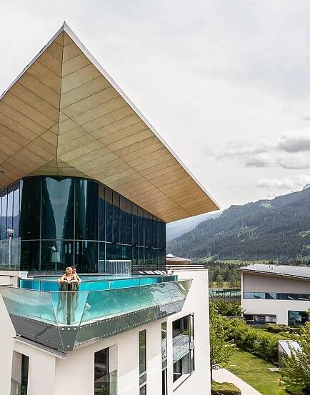 Woman in skyline pool on hotel roof with glass front in front of mountain panorama