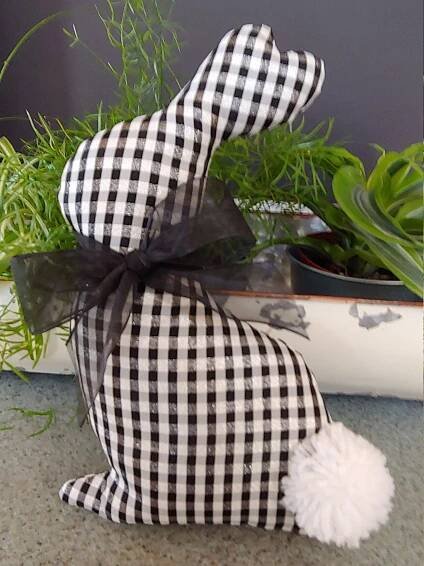 a black and white checkered bunny sitting next to some potted plants on the ground