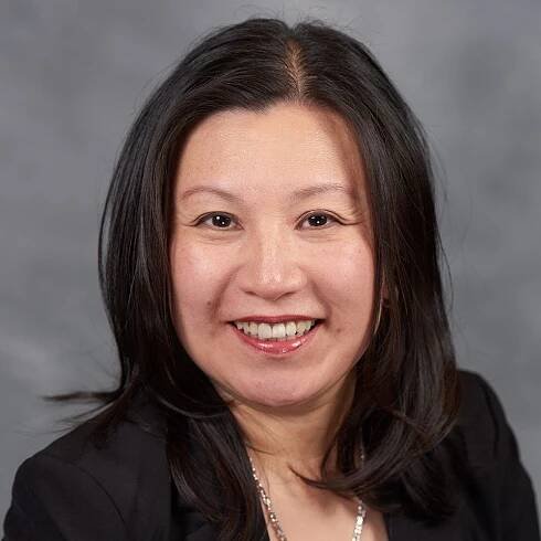 A woman in a black jacket and necklace is smiling for the camera.