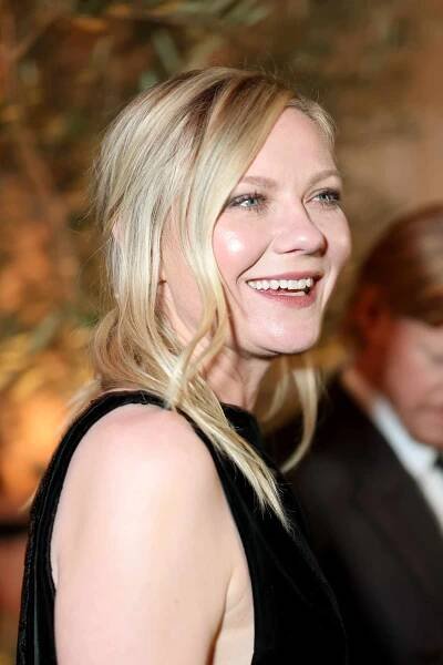 Kirsten Dunst smiling in a black dress at an event