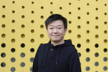 Image of Asian man wearing black hoodie standing in front of yellow background with black circles on it