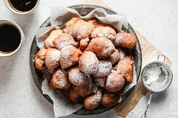 Doughnuts dusted with confectioners' sugar from a small wire mesh sieve