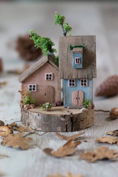 a small wooden house sitting on top of a piece of tree stump with leaves around it