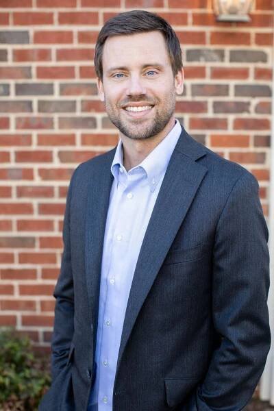 derrick- dawson-standing-in-front-of-a-brick-wall-in-a-suit