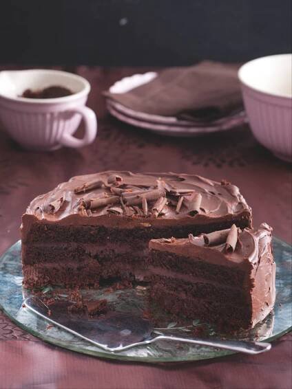 a piece of chocolate cake on a plate with one slice cut out and two cups in the background