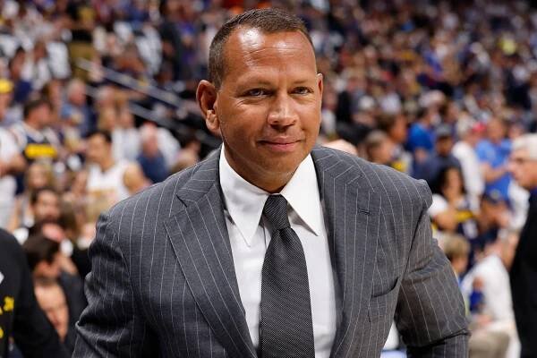 A-Rod poses for a photo in a suit and tie in front of a packed crowd at a basketball game