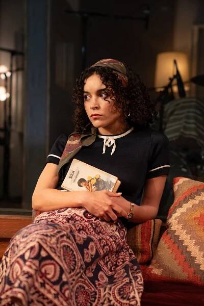 Juliana Canfield sitting on a couch, holding a book, looking away thoughtfully, wearing a casual out...