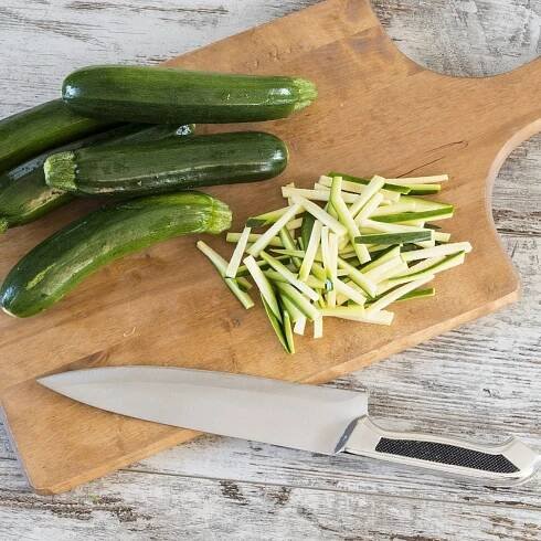 Julienne schneiden von Zucchini auf einem Holzbrett.