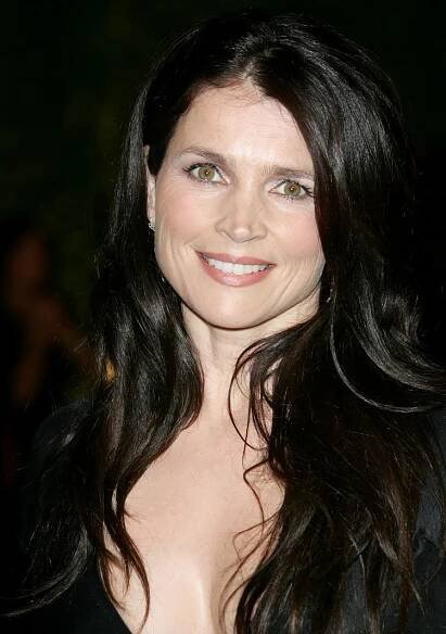 Julia Ormond smiling with a curly hairstyle and hazel eyes wearing a black v-neck dress