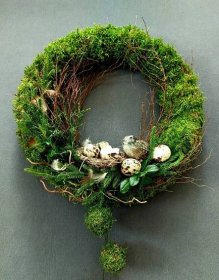 a moss wreath with birds and eggs on it sitting on a table in front of a gray wall