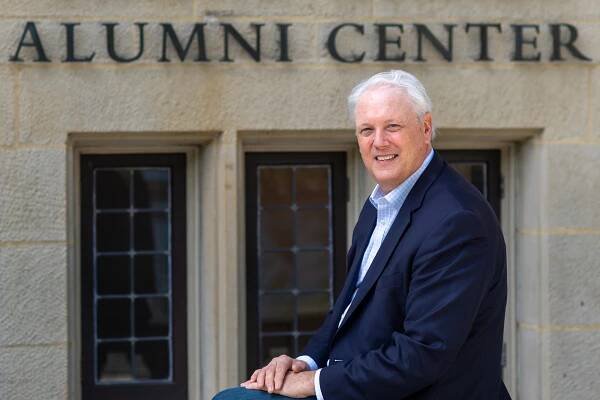 Steve Hall, VP in alumni relations who helped spearhead the hugely successful BU fund raising campaign, is retiring. Here he sits on one of the railings outside of the Dahod Family Alumni Center at the Castle on July 31, 2020. He wars a blue suits, and ornate windows are seen on the building behind hime with the sign "Dahod Family Alumni Center"