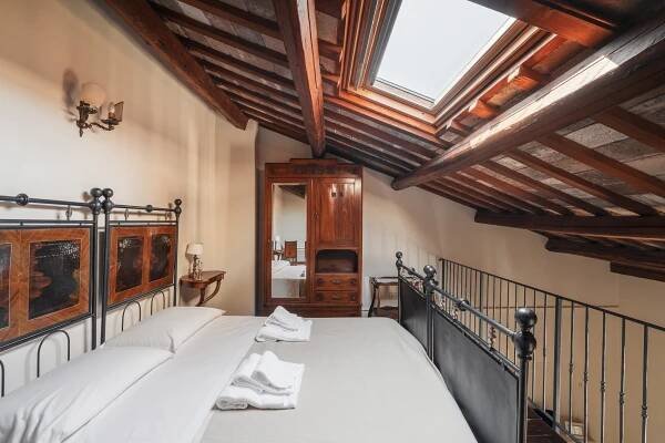 Double bedroom with wrought iron bed and antique wardrobe on a loft under the farmhouse roof, lit by a small skylight