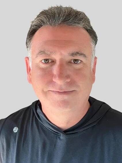 A headshot of a man smiling with silver hair wearing a black shirt