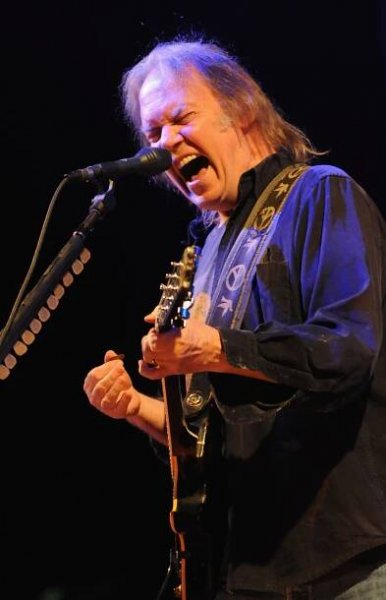 Neil Young performing on stage with a guitar.