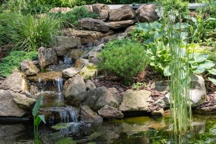Zahradní vodopád. Zahradní jezírka s vodou květy. Krásný rybník v zahradě uprostřed kamene během. — Stock fotografie