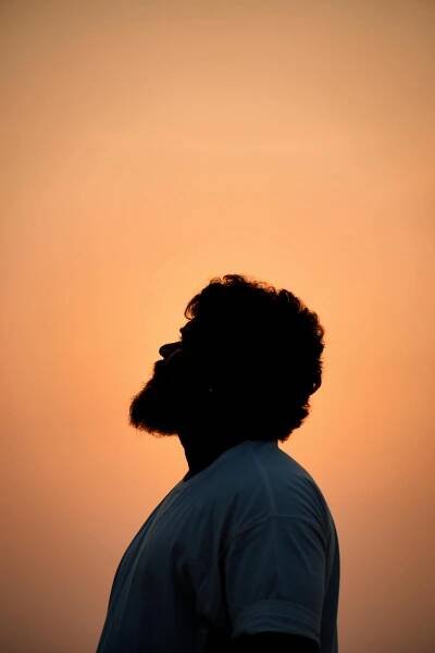 Free Silhouette of a bearded man gazing upwards against a vibrant sunset sky backdrop. Stock Photo
