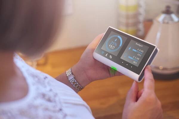 Homeowner checking current energy costs on smart meter in the kitchen of her home