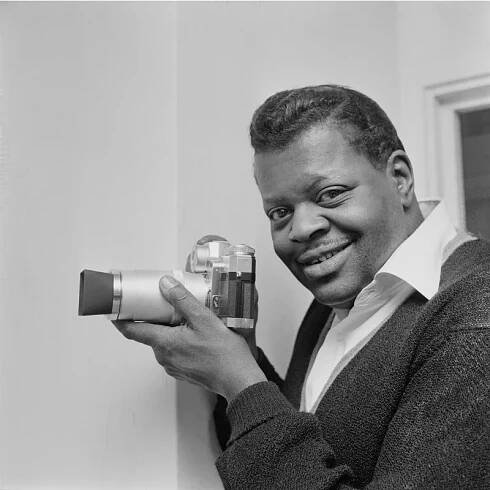 Canadian jazz pianist and composer Oscar Peterson (1925 - 2007) holding a camera, UK, 22nd February 1963
