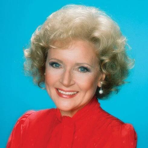 an older woman with blonde hair wearing a red shirt and smiling at the camera, against a blue background