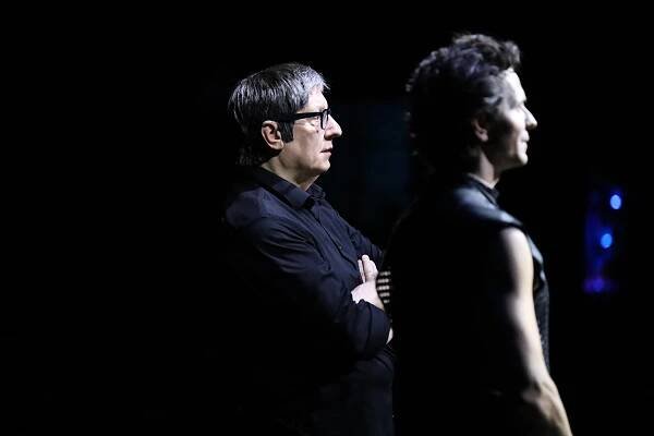 Robert Lepage, in a black long0sleeved shirt, stands in profile at left, facing right. He wears dark horn-rimmed glasses. Next to him in a sleeveless dark tunic, also looking to the right, is Guillaume Côté.
