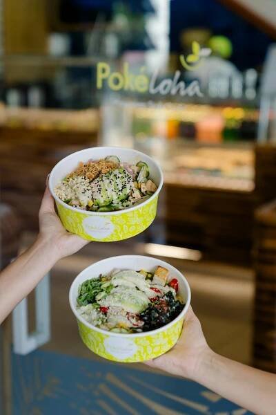 Free Two hands holding colorful poke bowls at the entrance of Pokeloha restaurant. Stock Photo