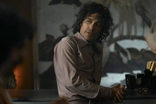 martin rodriguez as jorge rivi ayala in griselda. he's a man with curly hair, worn long, in a nice looking mauve shirt