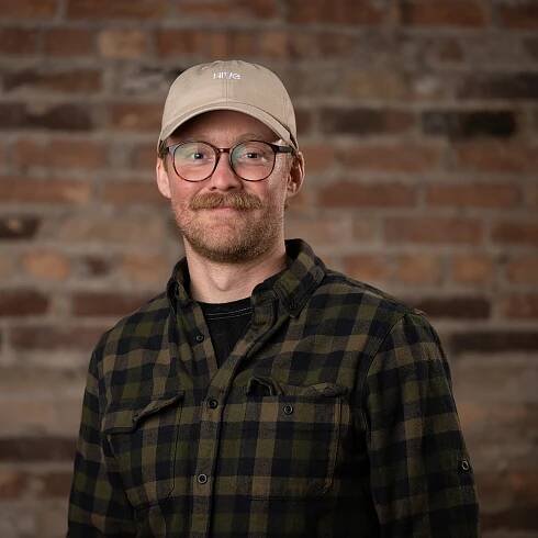 Ian Roberts, Hive CEO and Co-founder, smiling with a beard and glasses, wearing a dark t-shirt, standing against a light-colored wall.