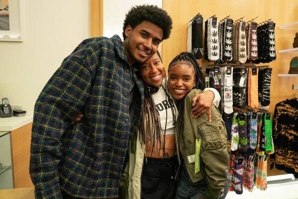 Three people smiling and hugging in a store. They are standing in front of shelves displaying various patterned socks. Casual and cozy styling