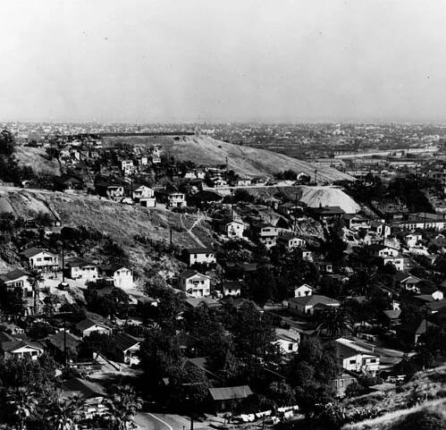 An overhead black and white image shows houses dotting a hillside.