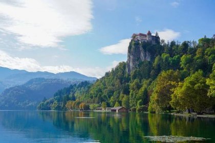 Pictured: Lake Bled with castle up on a cliff in the background, surrounded by trees. 